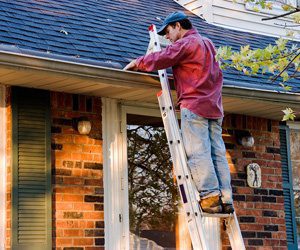 A man on a ladder cleaning a gutter