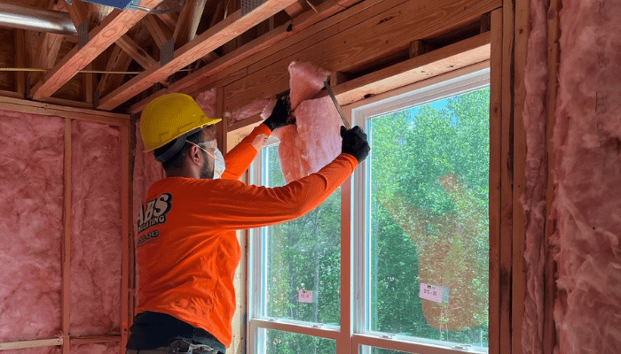 An ABS employee installing fiberglass insulation in a wall